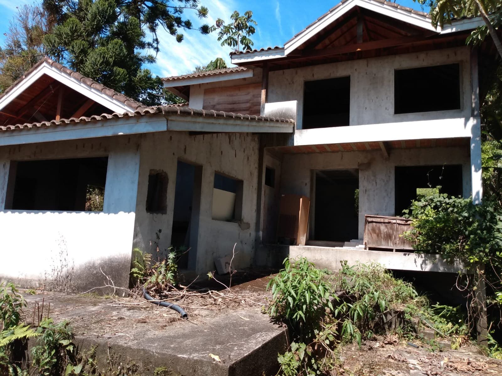 Casa em estrutura de concreto aparente, sem esquadrias, com vegetação crescida ao redor