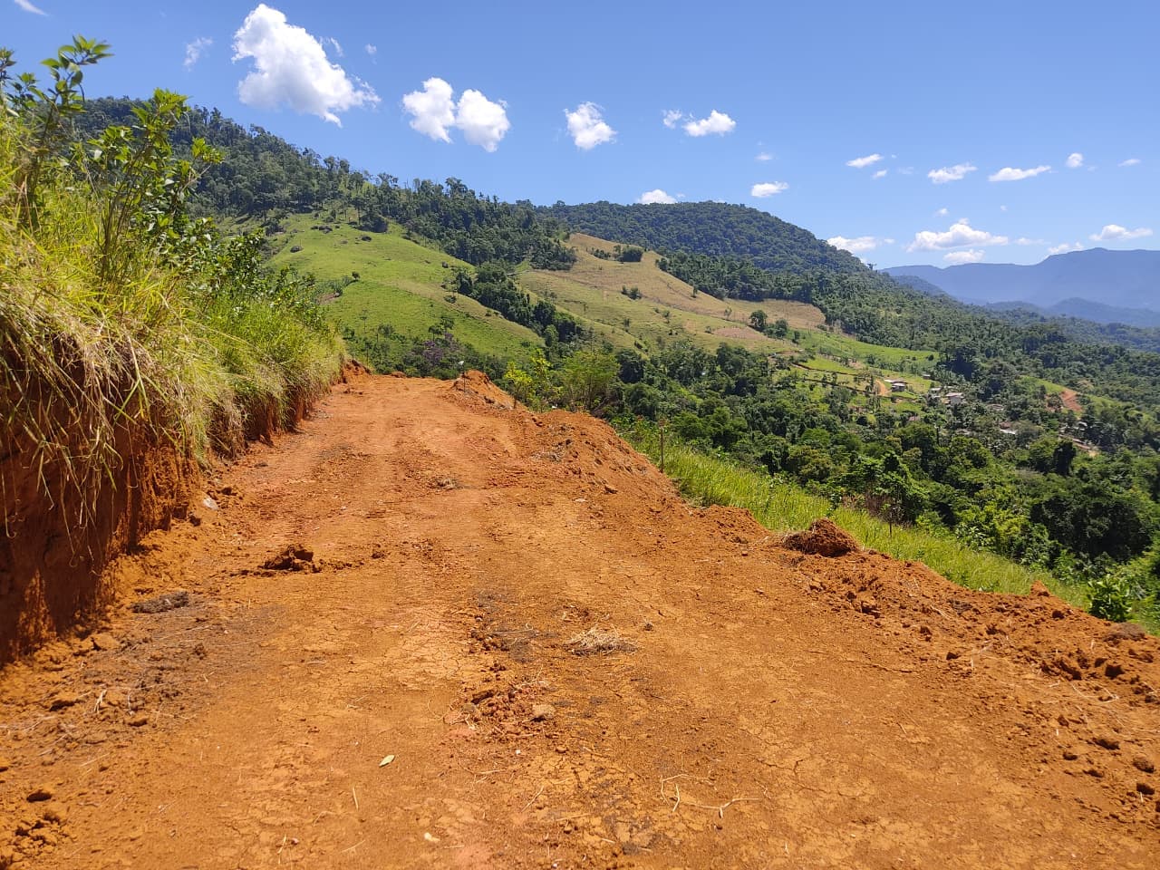 Plataforma da estrada aberta em terra vermelha acompanhando a encosta, com o vale ao fundo