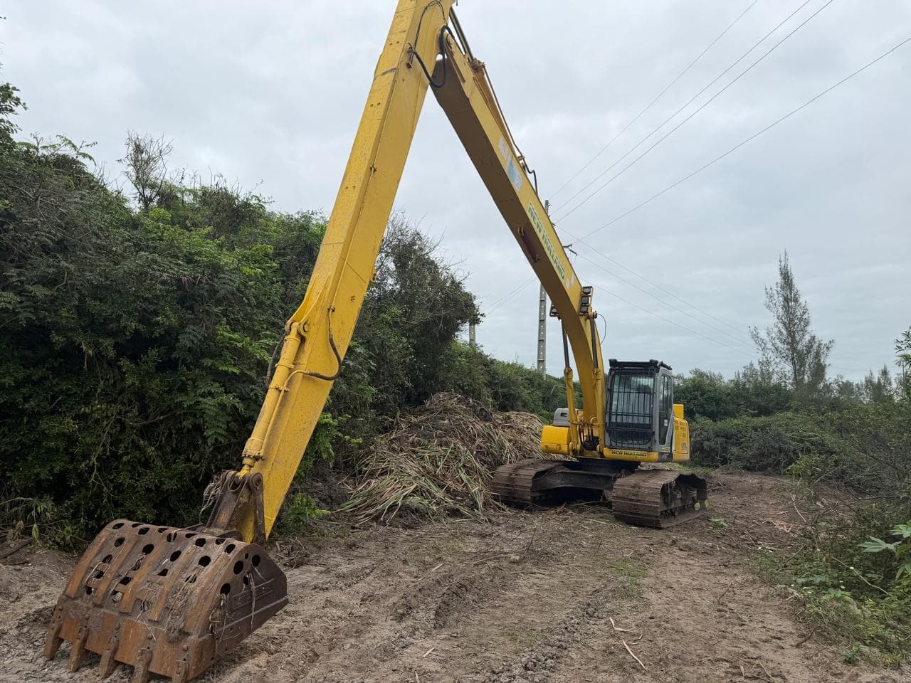 Escavadeira de alcance longo com a lança estendida sobre a área em limpeza