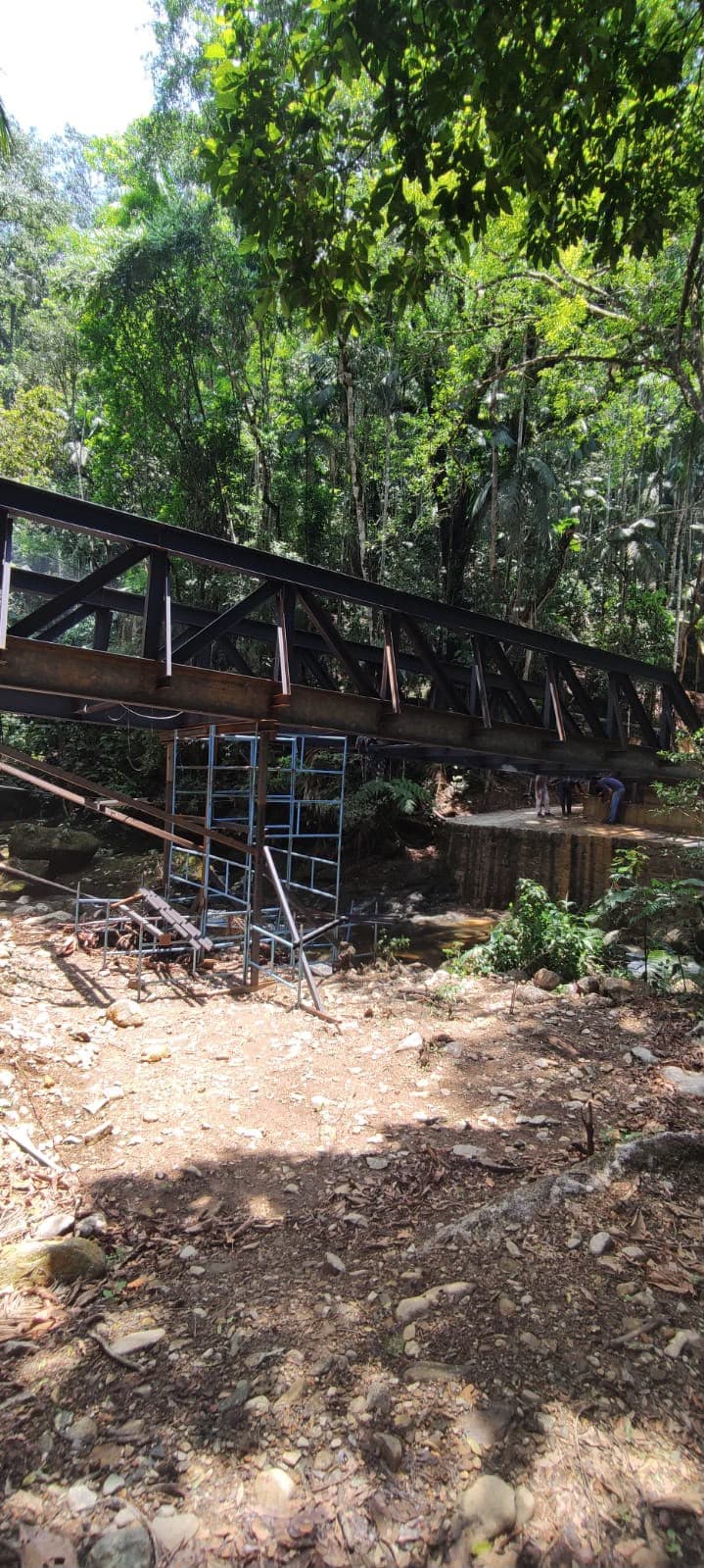 Treliça metálica da ponte apoiada sobre escoramento, atravessando o córrego em meio à mata