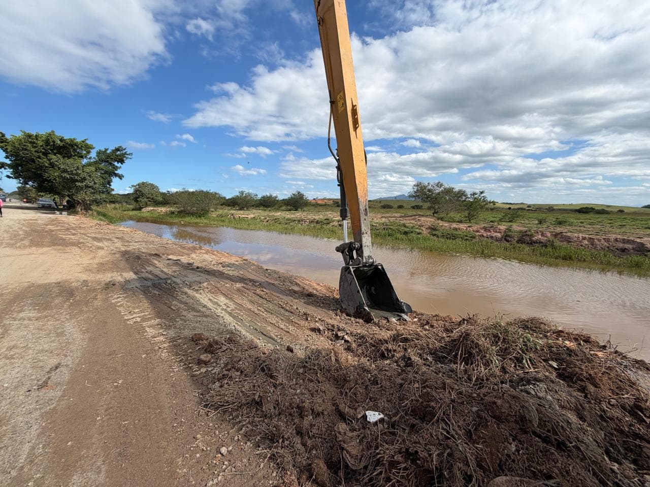 Concha da escavadeira retirando material da margem de um canal alagado